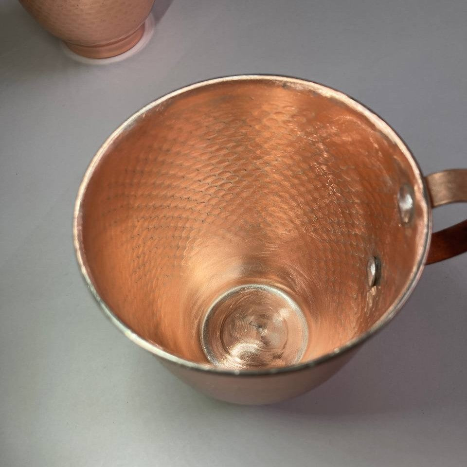 A copper-colored metal mug with a hammered texture on the inside, shown from a top-down angle on a gray surface.