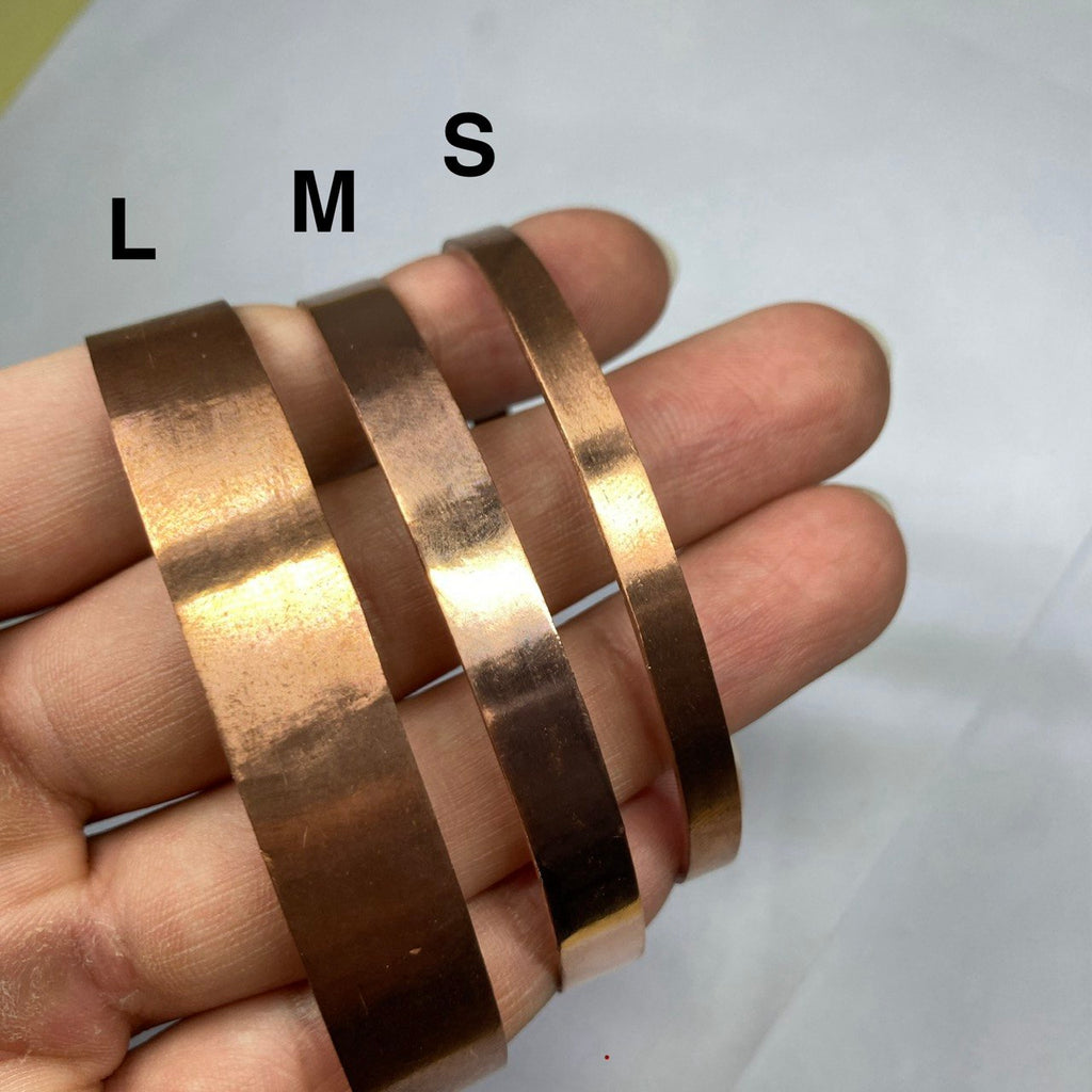 Three copper bands labeled L, M, S held in a hand against a white background