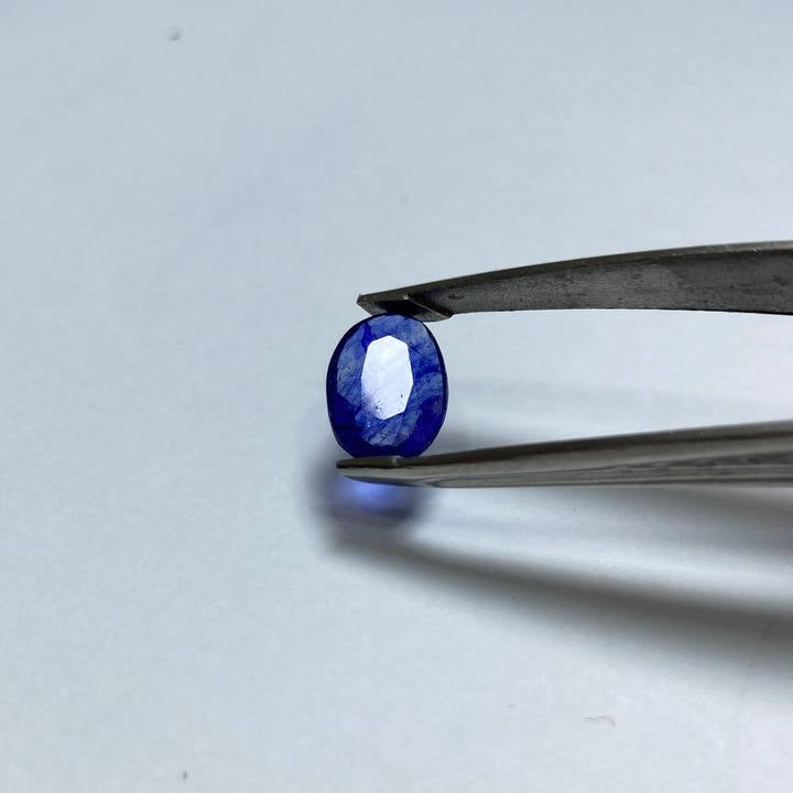 Blue gemstone held by tweezers on a white background
