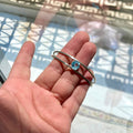 Hand holding a silver bracelet with a blue topaz gemstone in front of a reflective glass surface.