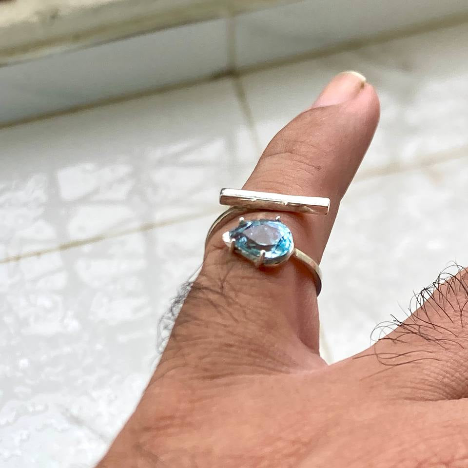Hand wearing a silver ring with a blue gemstone on a tiled floor background