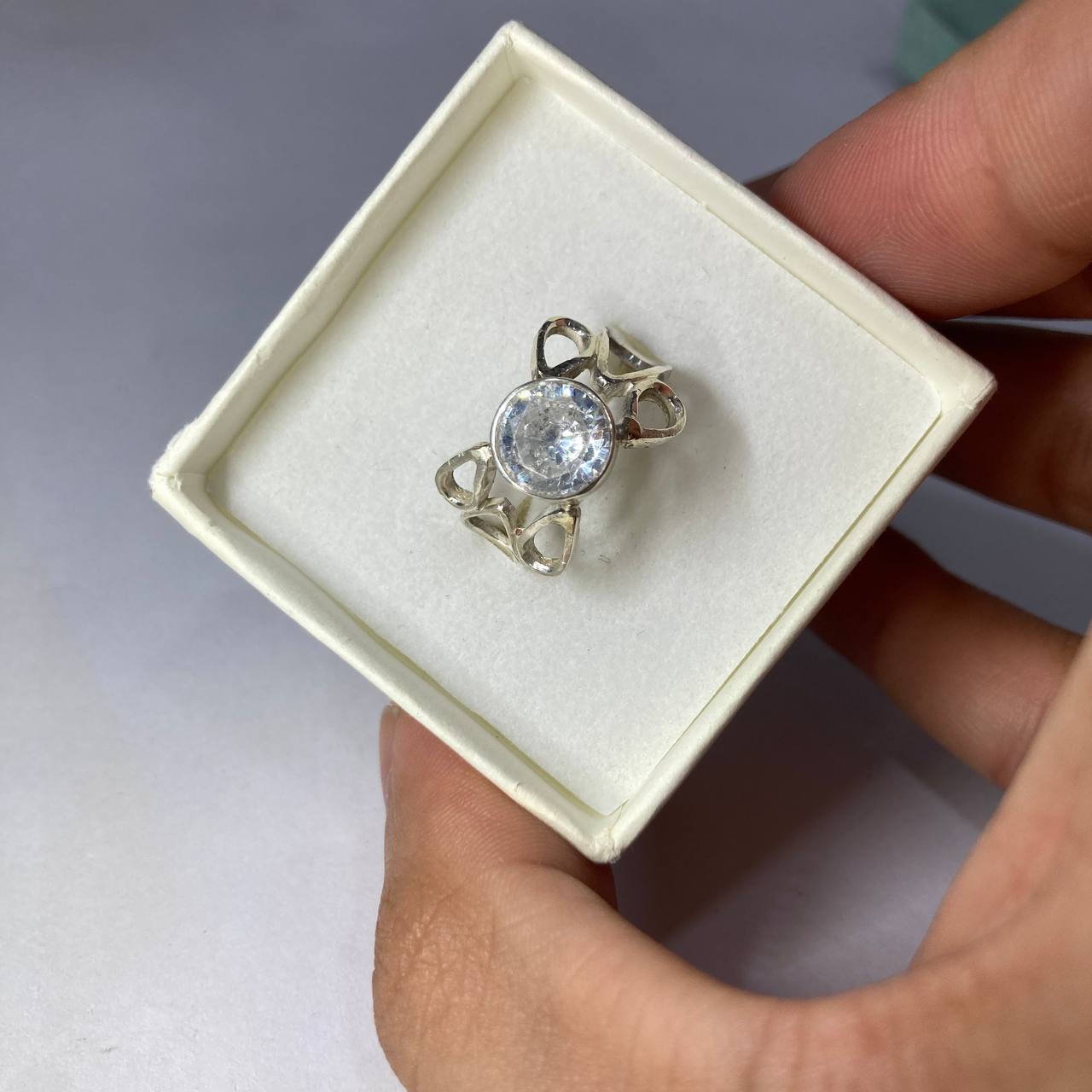 Silver ring with a large gemstone in a white box held by a hand.