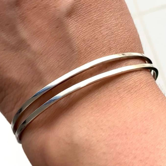 Silver bangles on a wrist with a neutral background