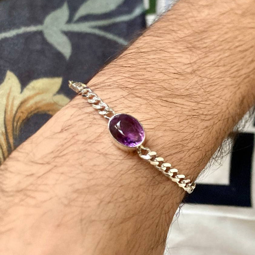 silver bracelet with a purple gemstone on a wrist against a patterned fabric background