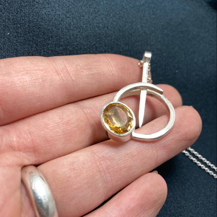 Silver pendant with a yellow gemstone held in a hand against a dark background