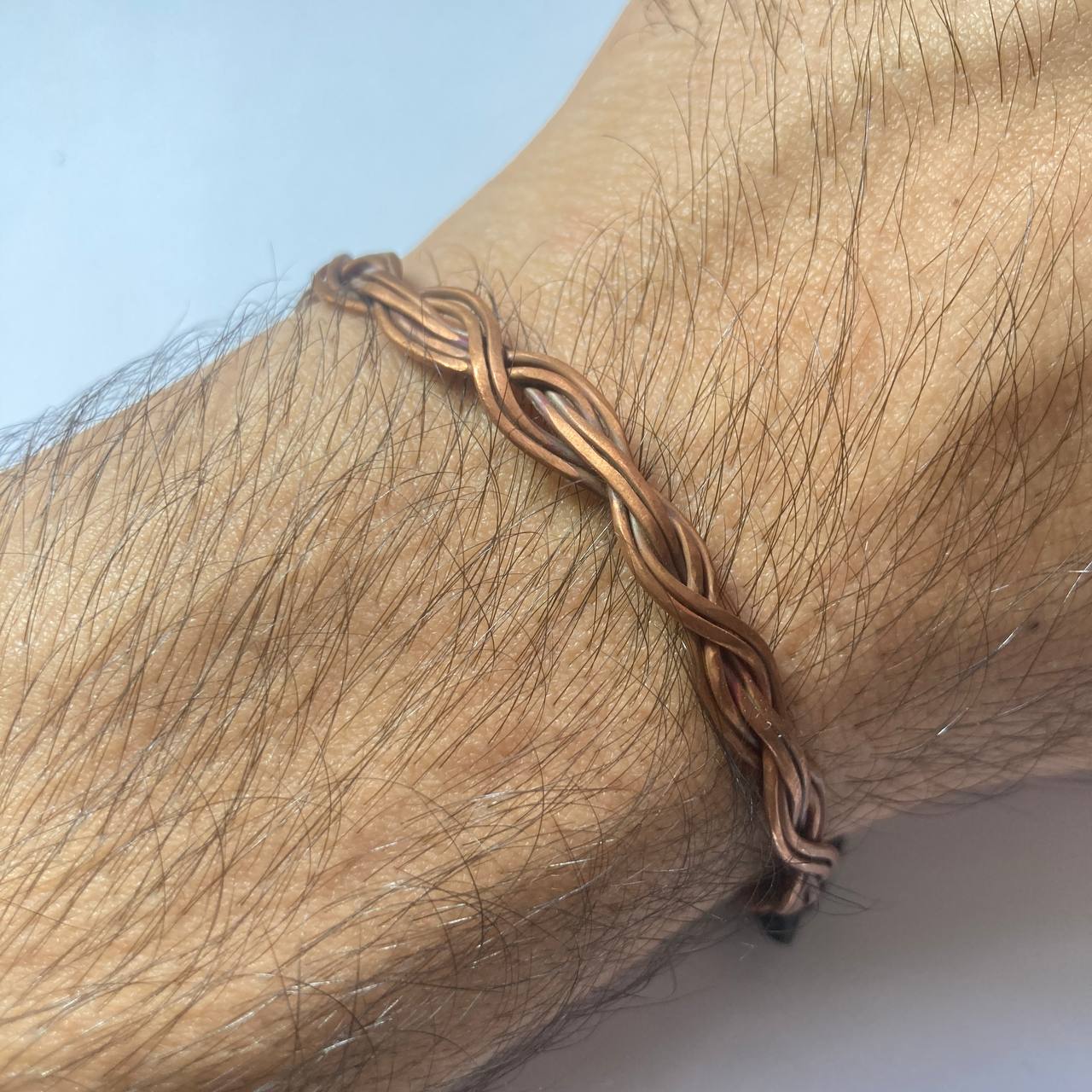 A close-up of a person's wrist wearing a braided copper bracelet.