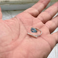 Silver ring with a blue gemstone held in a hand against a blurred background