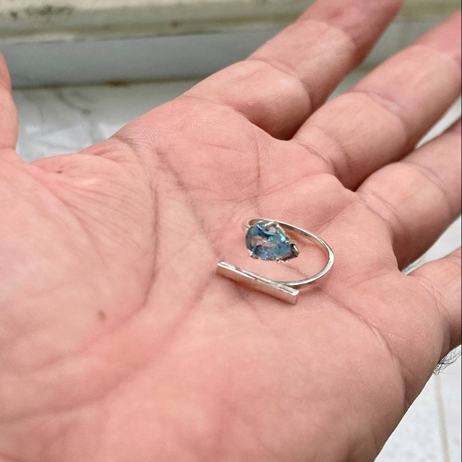 Silver ring with a blue gemstone held in a hand against a blurred background