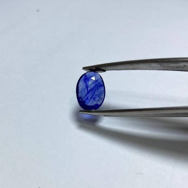 Blue gemstone held by tweezers on a white background