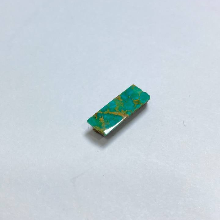 Small rectangular object with green and gold pattern on a white background