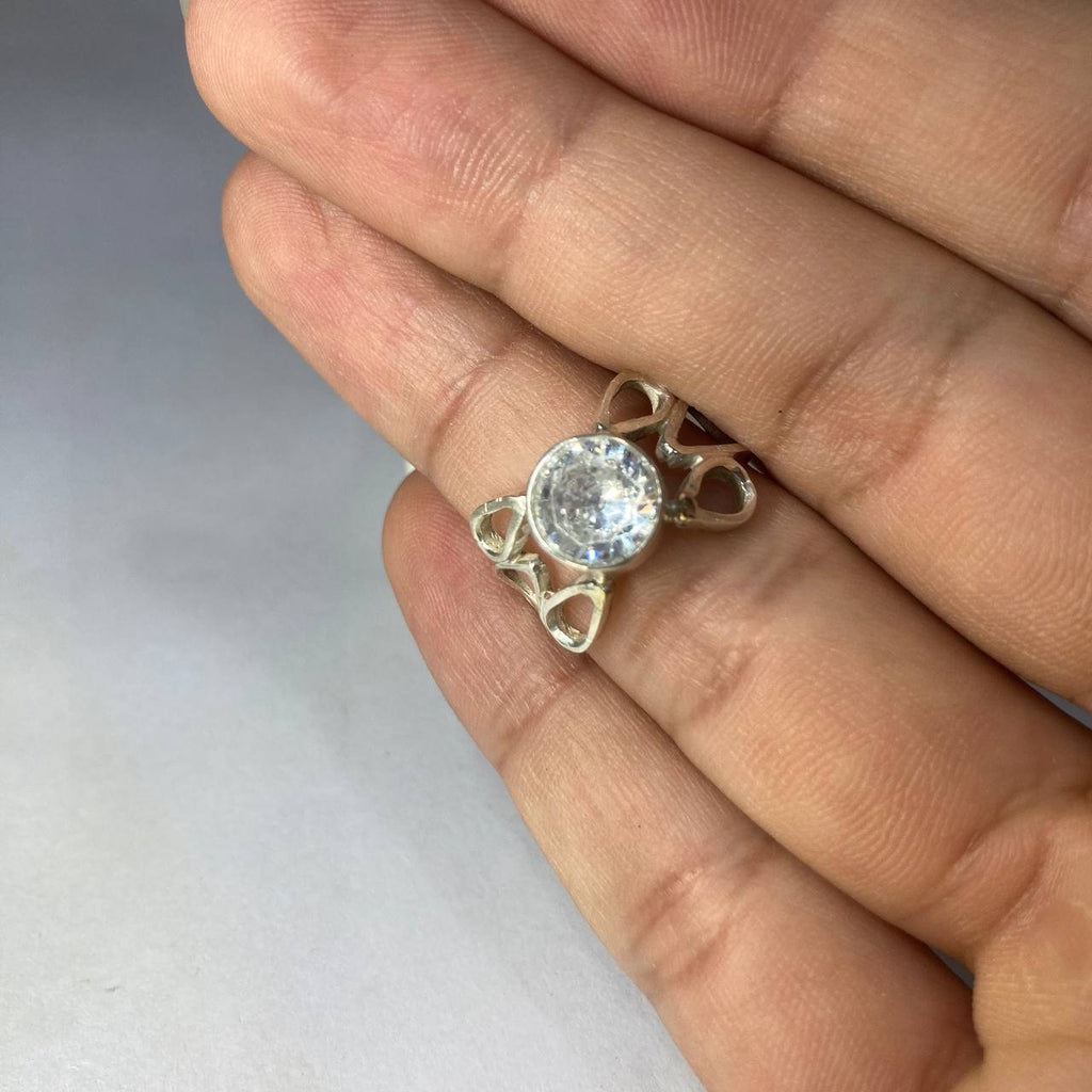 Silver ring with a clear gemstone held between fingers on a light background