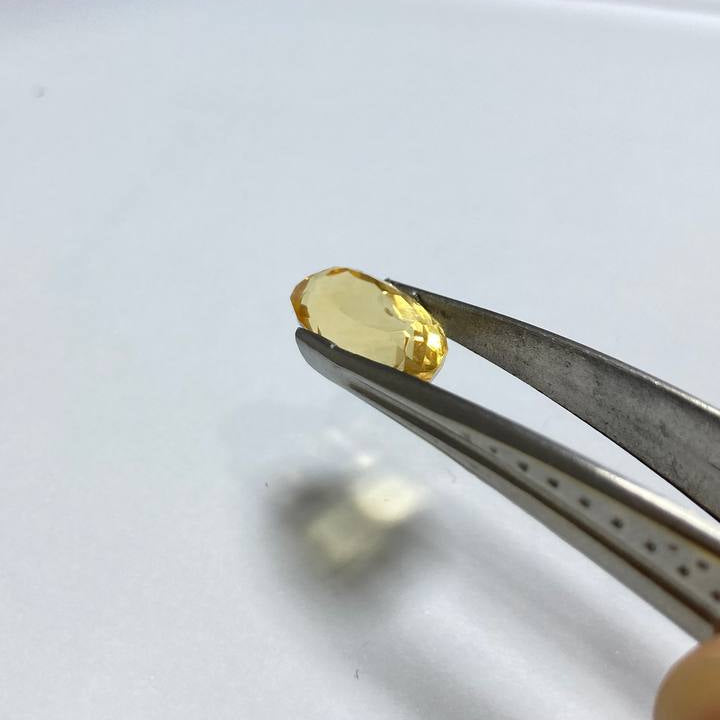 Yellow gemstone held by tweezers on a white surface