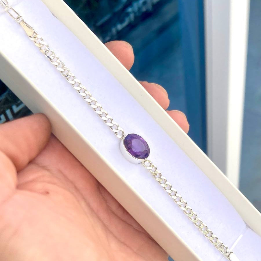 Silver bracelet with a purple gemstone held by a hand against a blurred indoor background