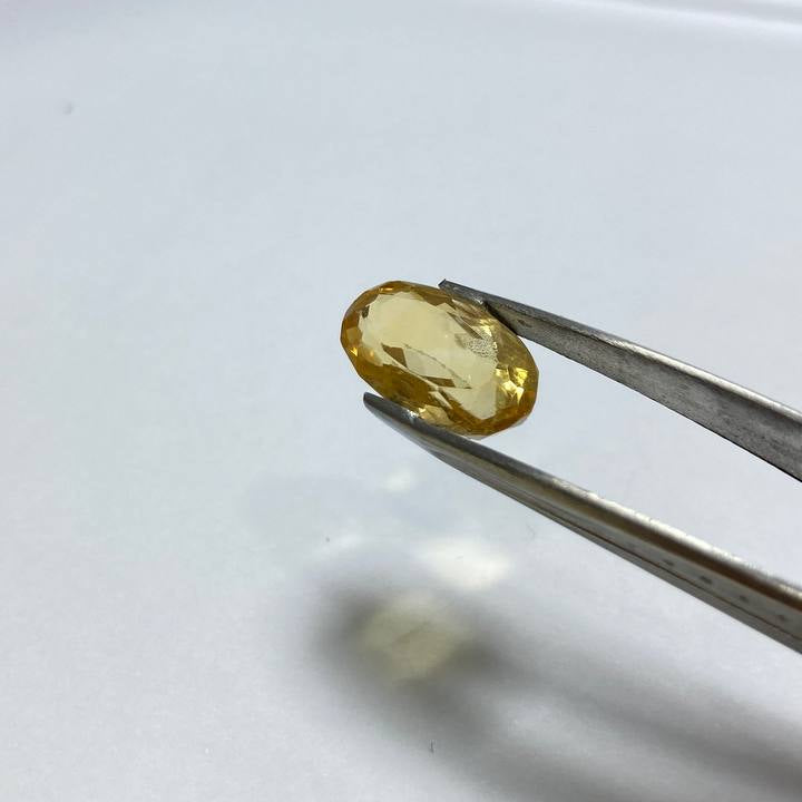 Yellow gemstone held by tweezers on a white background