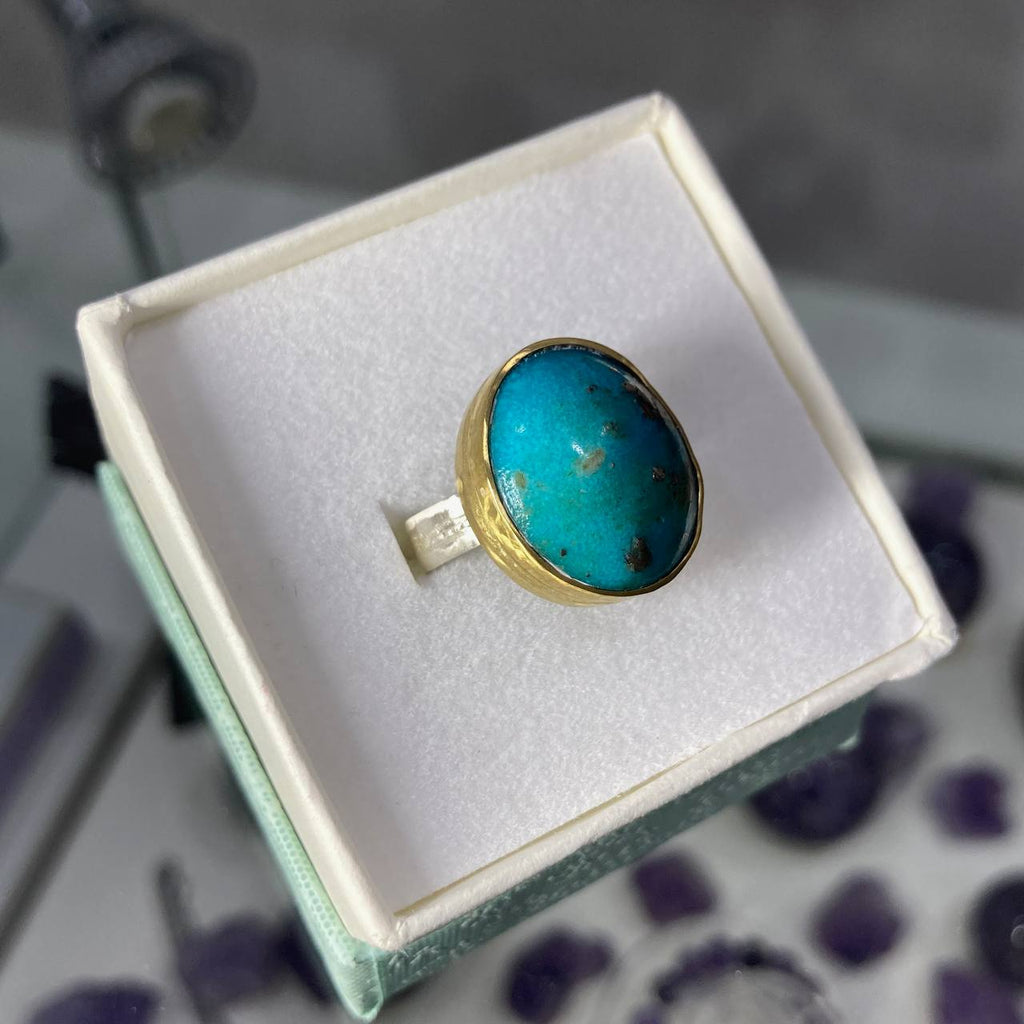 Turquoise ring in a brass setting on a white cushion in a jewelry box.