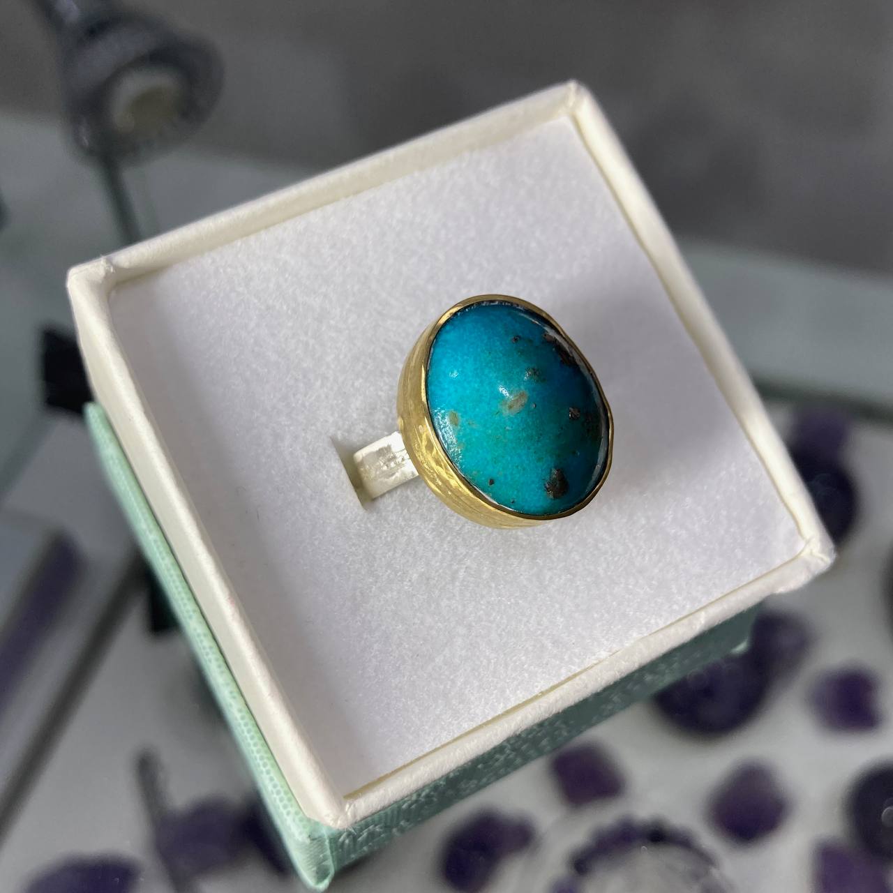 Turquoise ring in a brass setting on a white cushion in a jewelry box.
