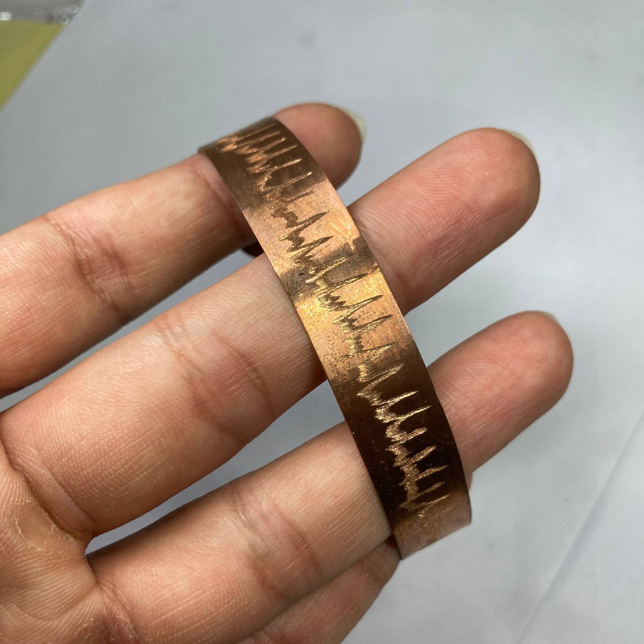 Hand holding a bronze bracelet with a textured pattern against a white background
