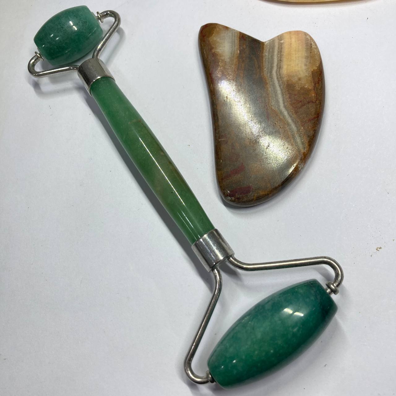 Green jade roller and gua sha tool on a white background