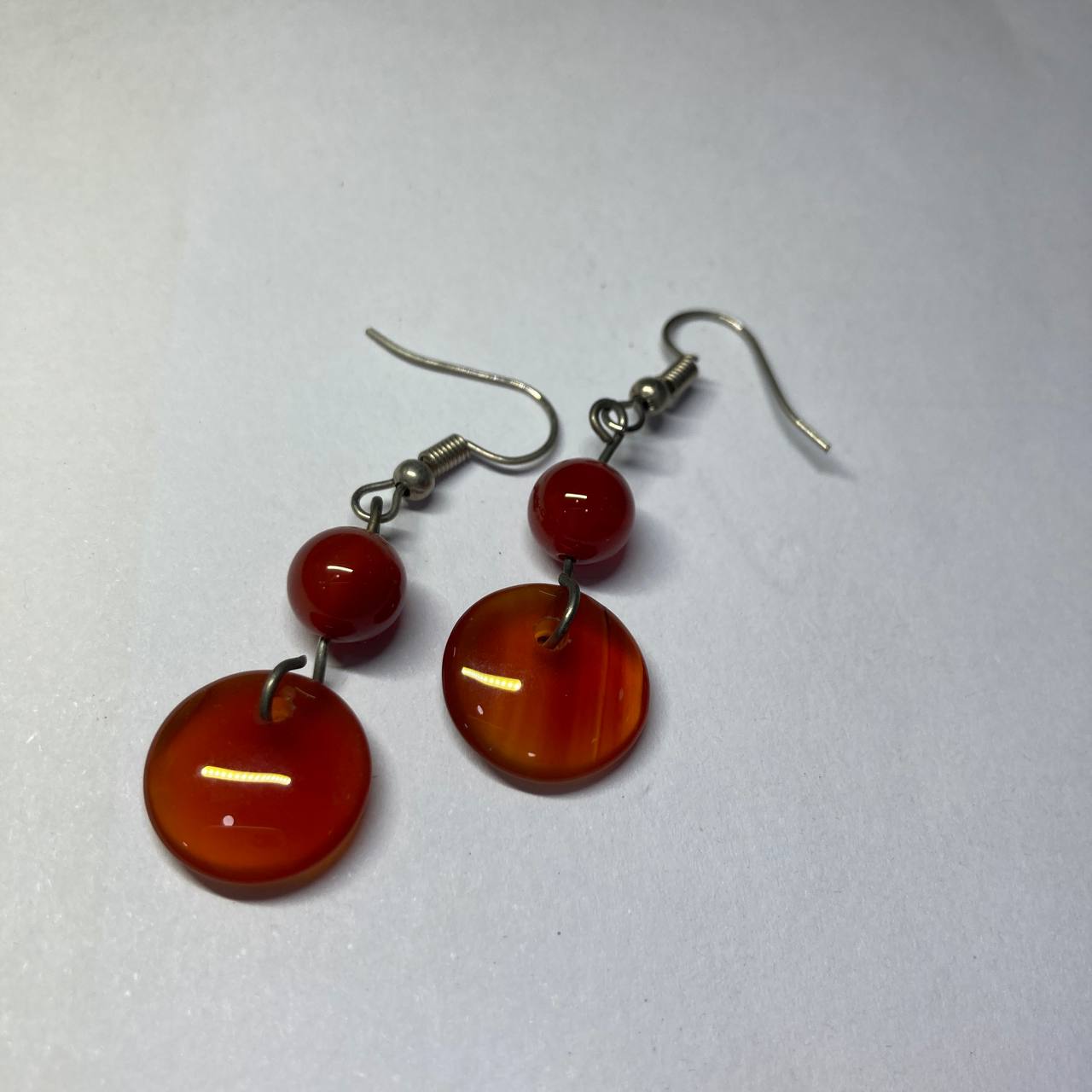 Pair of earrings with red and orange circular beads on a white background