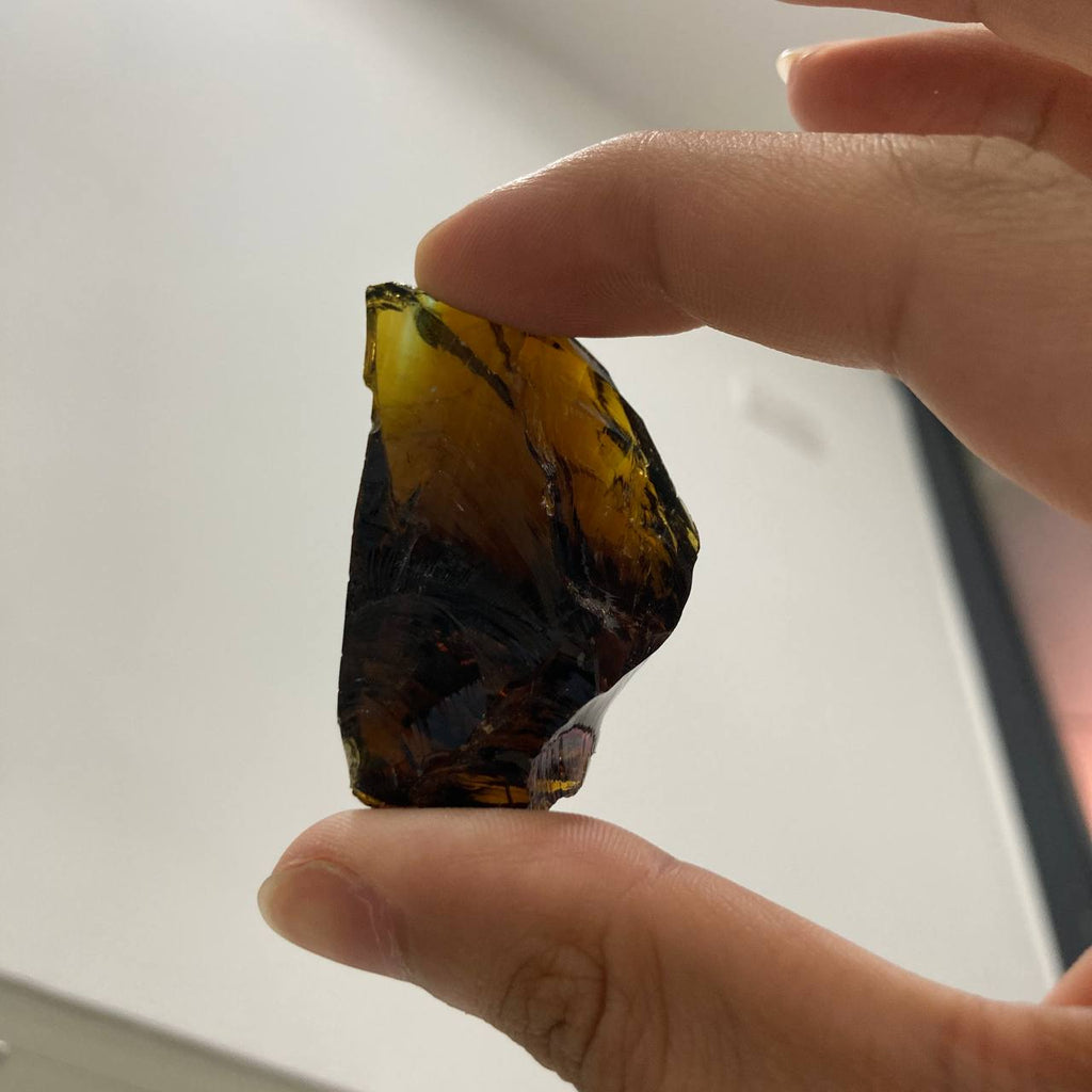Hand holding a rough piece of amber color obsidian against a neutral background