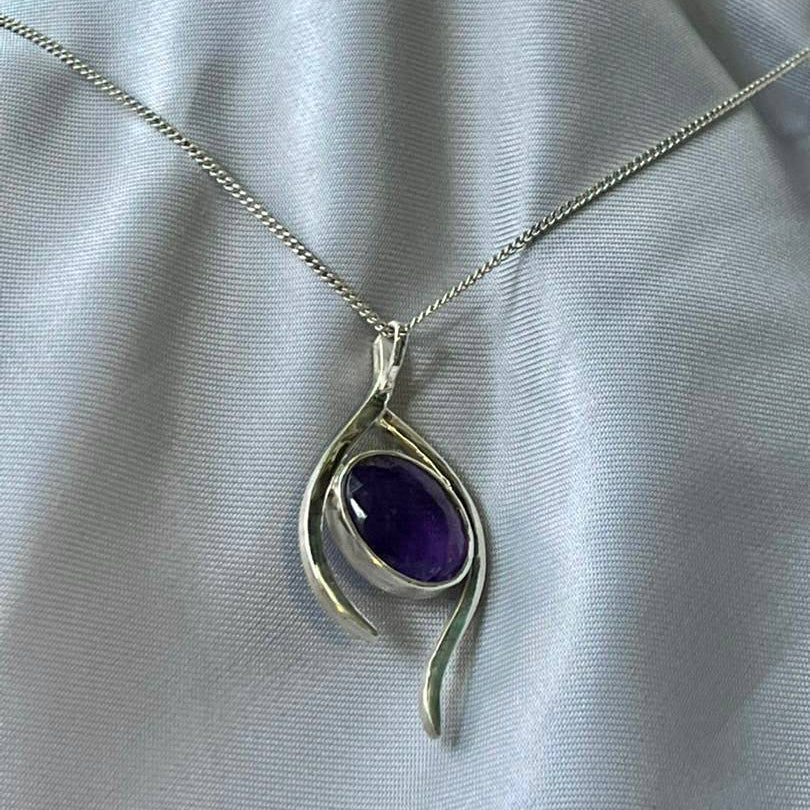 Silver pendant with a purple gemstone on a light gray fabric background
