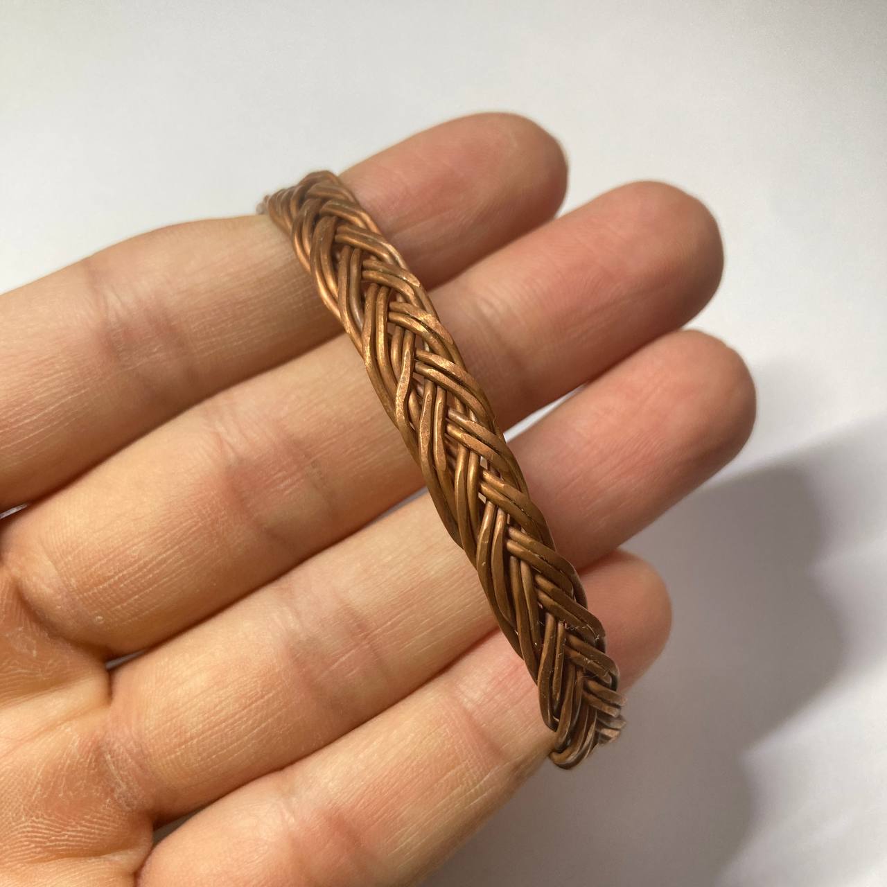 A close-up of a hand holding a braided copper bracelet against a plain white background.