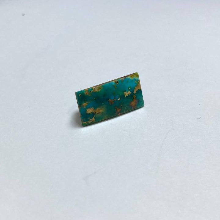 Small green rectangular object with gold specks on a white surface