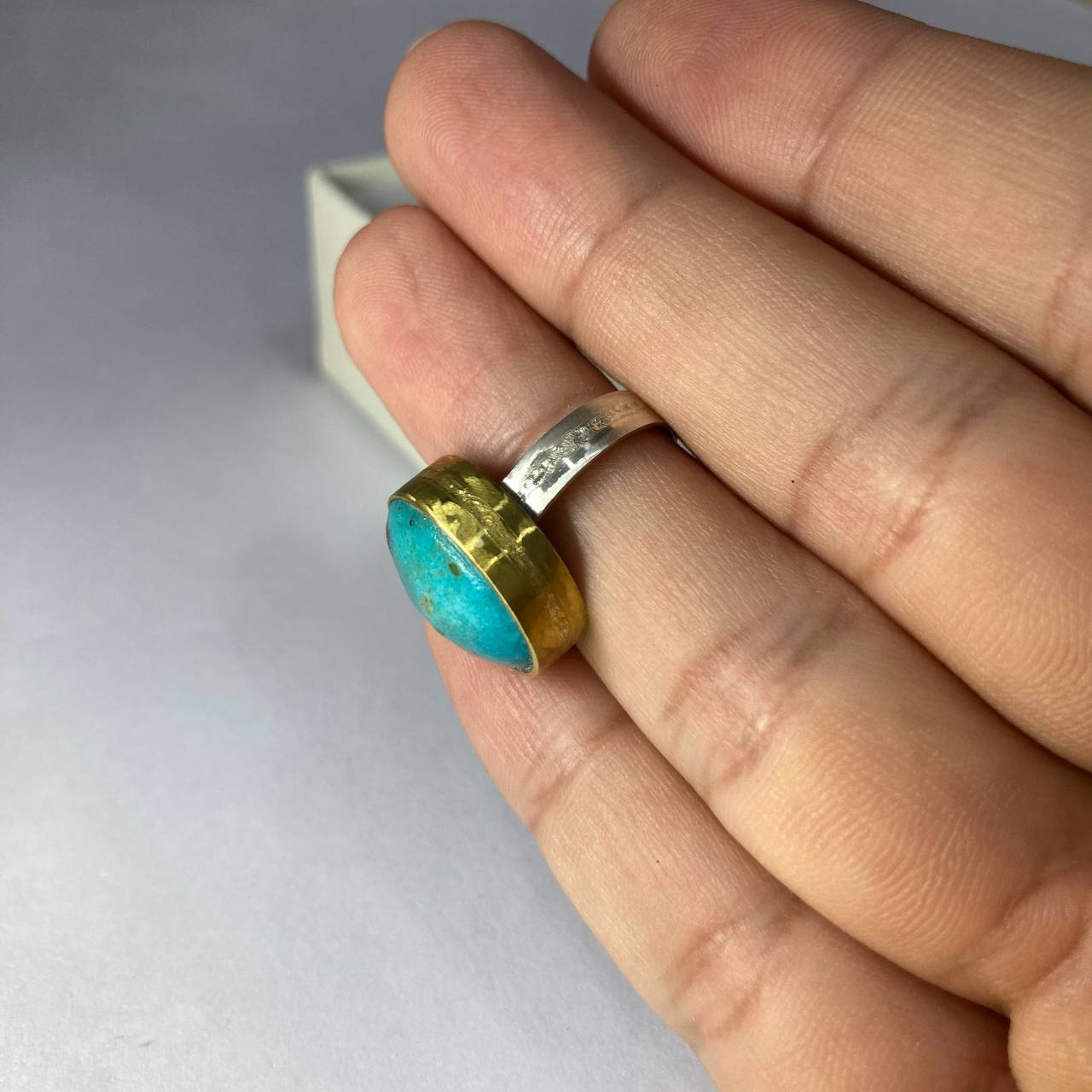 silver-brass ring with a turquoise stone on a finger against a neutral background