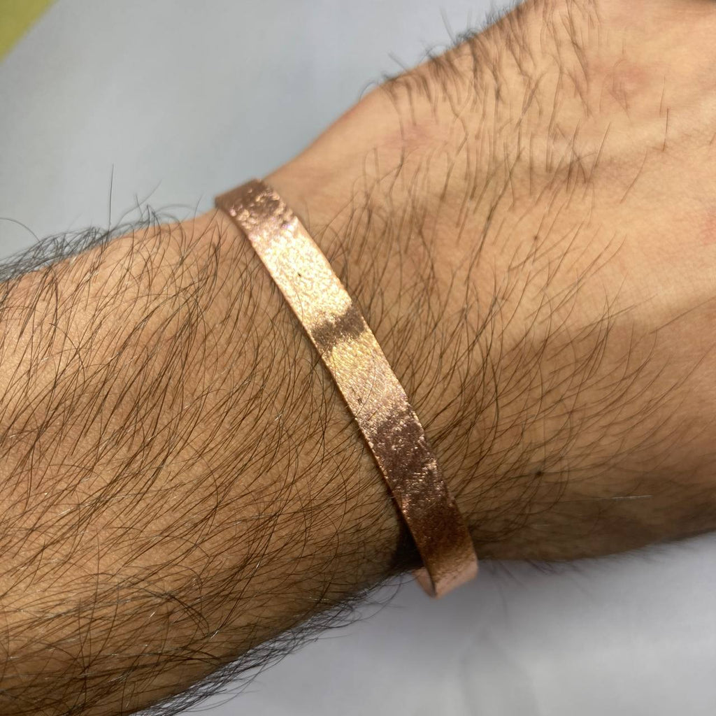 Copper bracelet on a wrist with a plain background