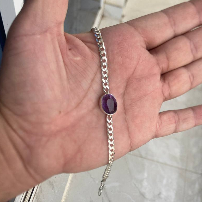 Hand wearing a silver chain bracelet with a purple gemstone on a marble floor.