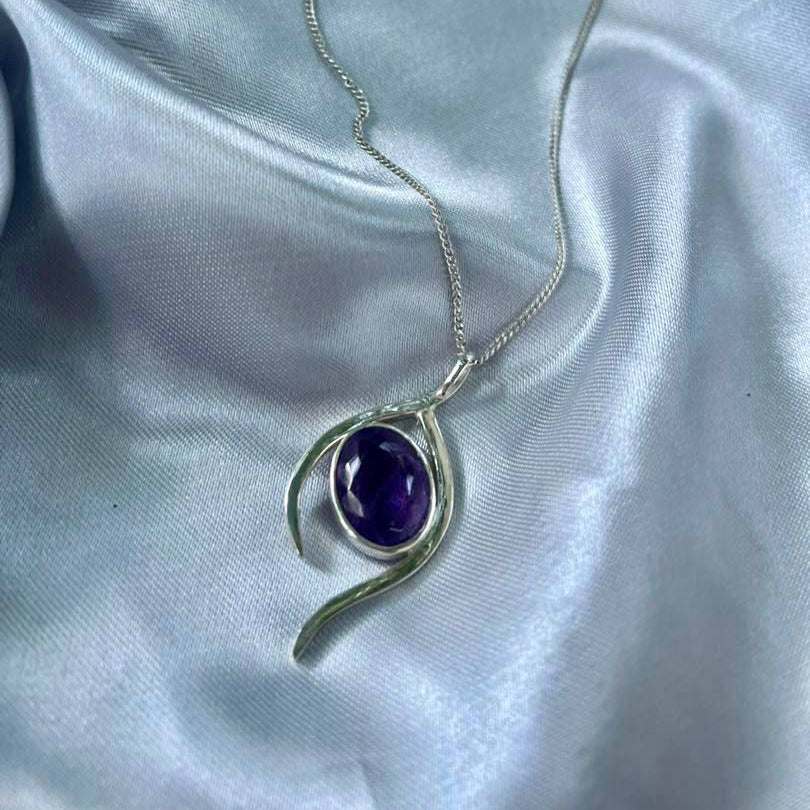 Silver necklace with a purple gemstone pendant on a satin surface