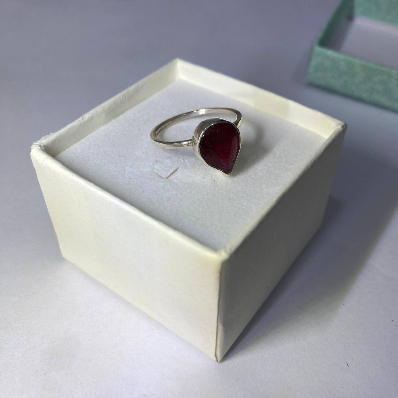Silver ring with a red gemstone in a white box on a gray surface