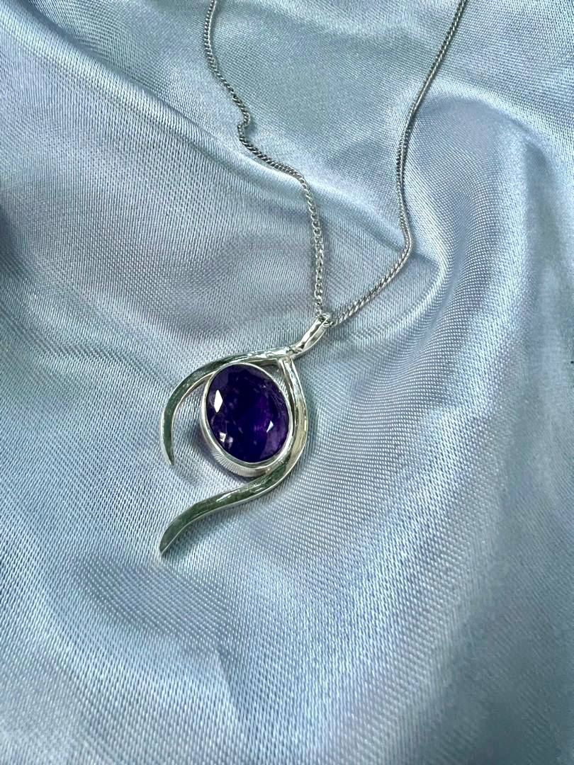 Silver pendant with a purple gemstone on a light blue fabric background
