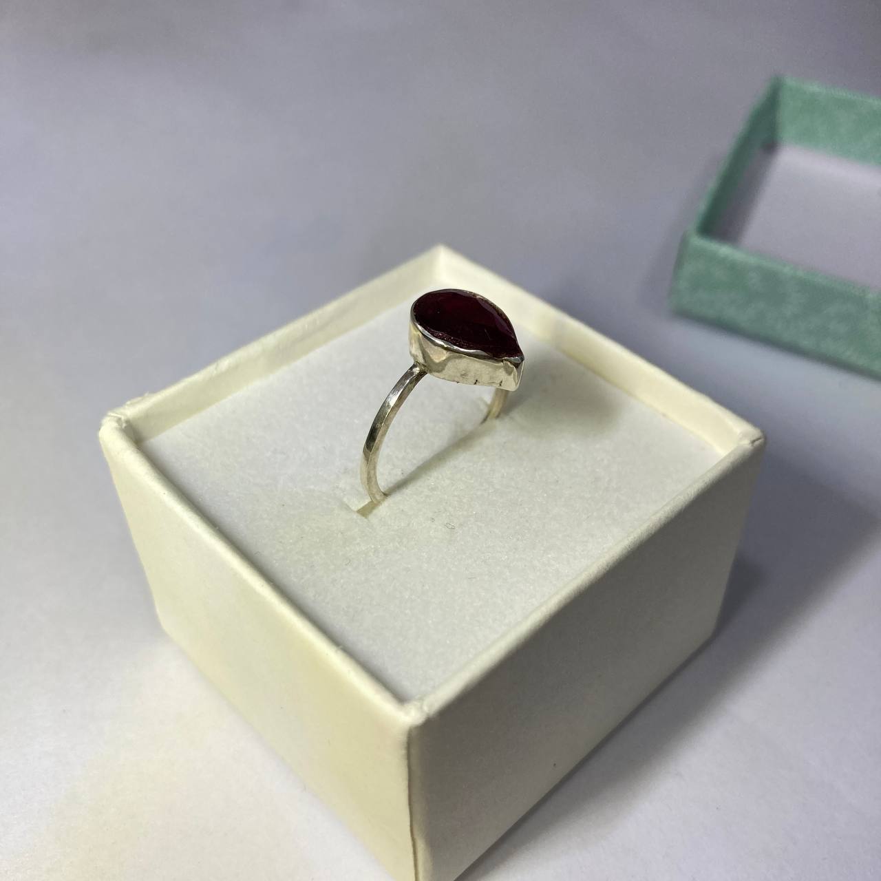 Silver ring with a red stone in a white box on a gray background