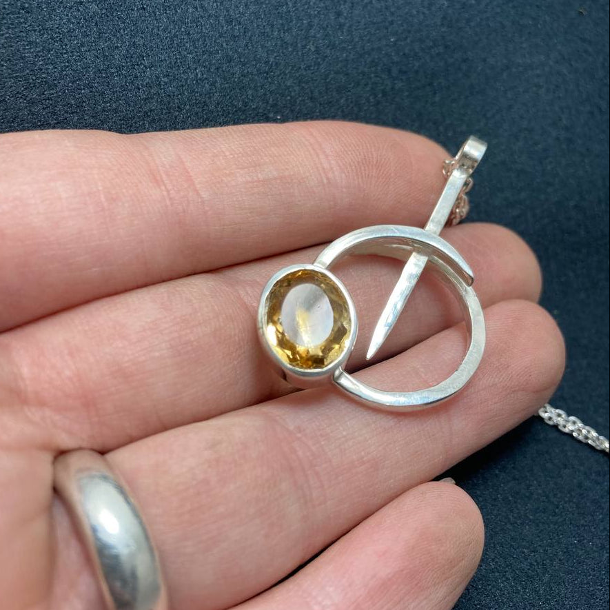 Silver pendant with a yellow gemstone held in a hand against a dark background