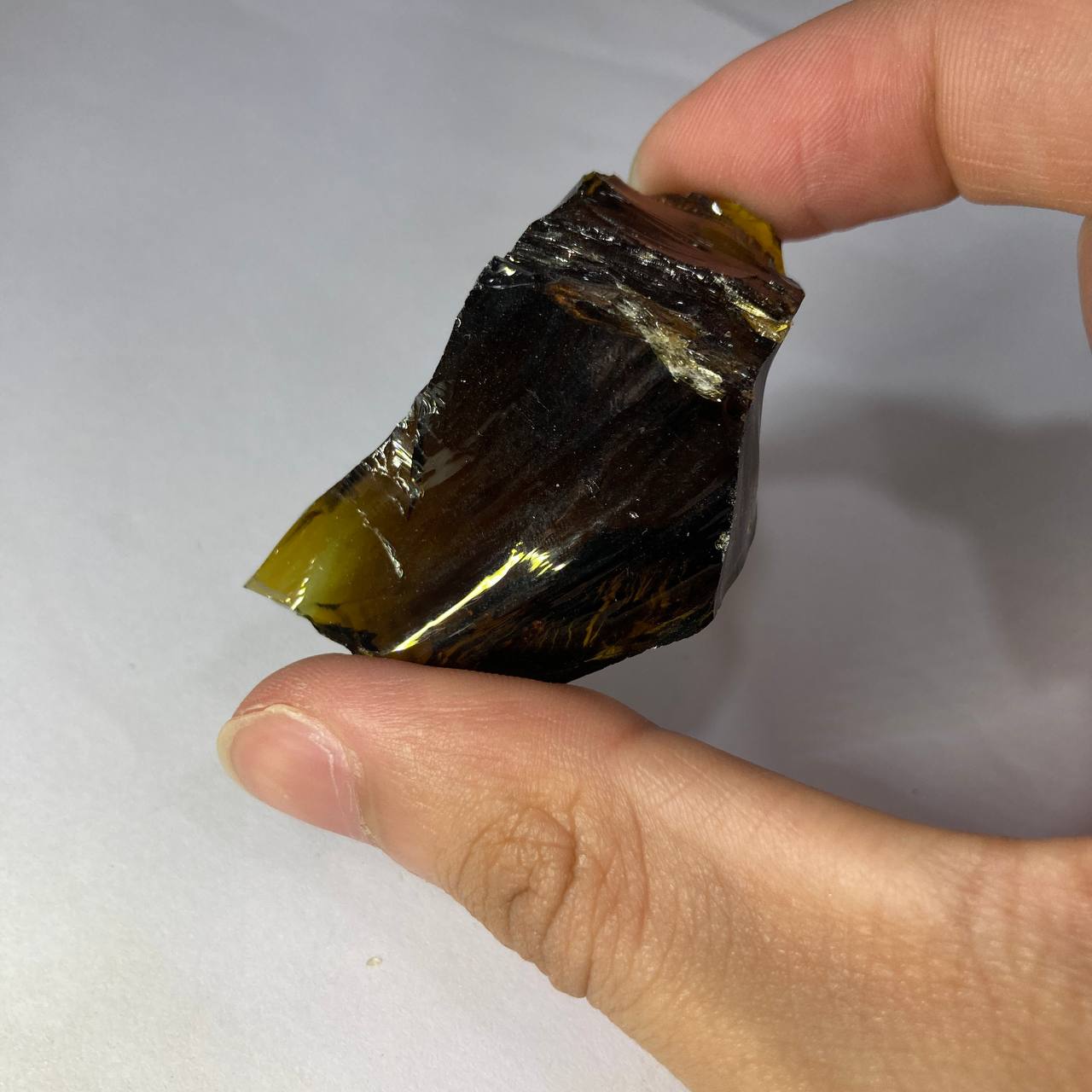 Hand holding a dark yellow crystal against a white background