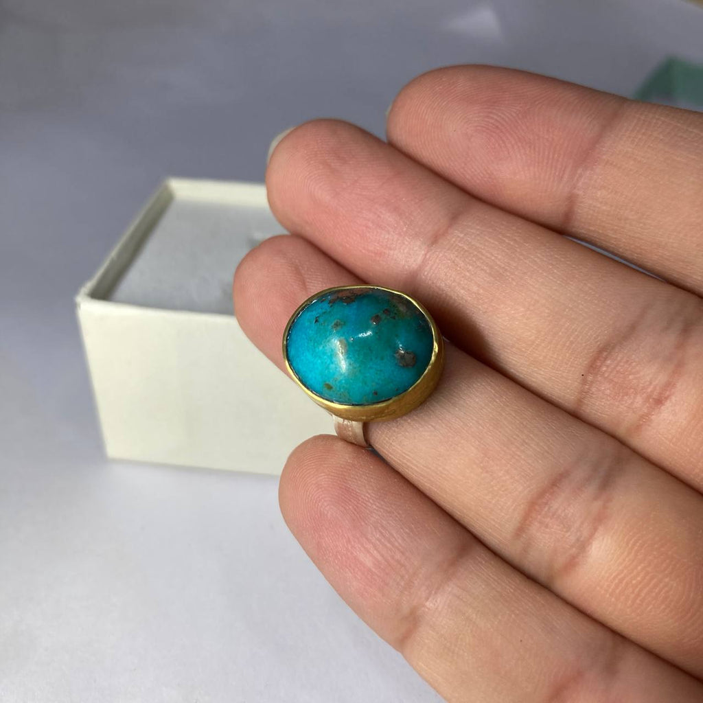 silver-brass ring with a turquoise stone on a finger against a neutral background