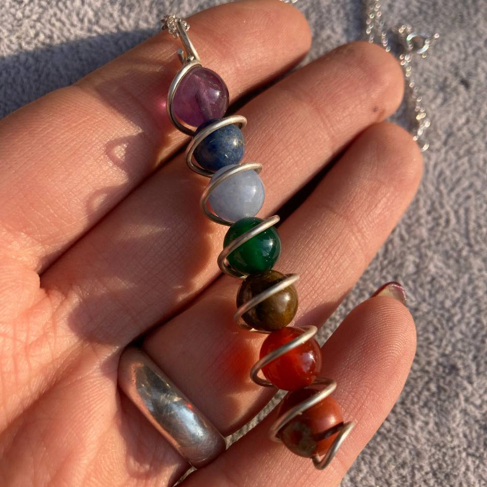 Hand holding a necklace with colorful beaded pendants on a neutral background