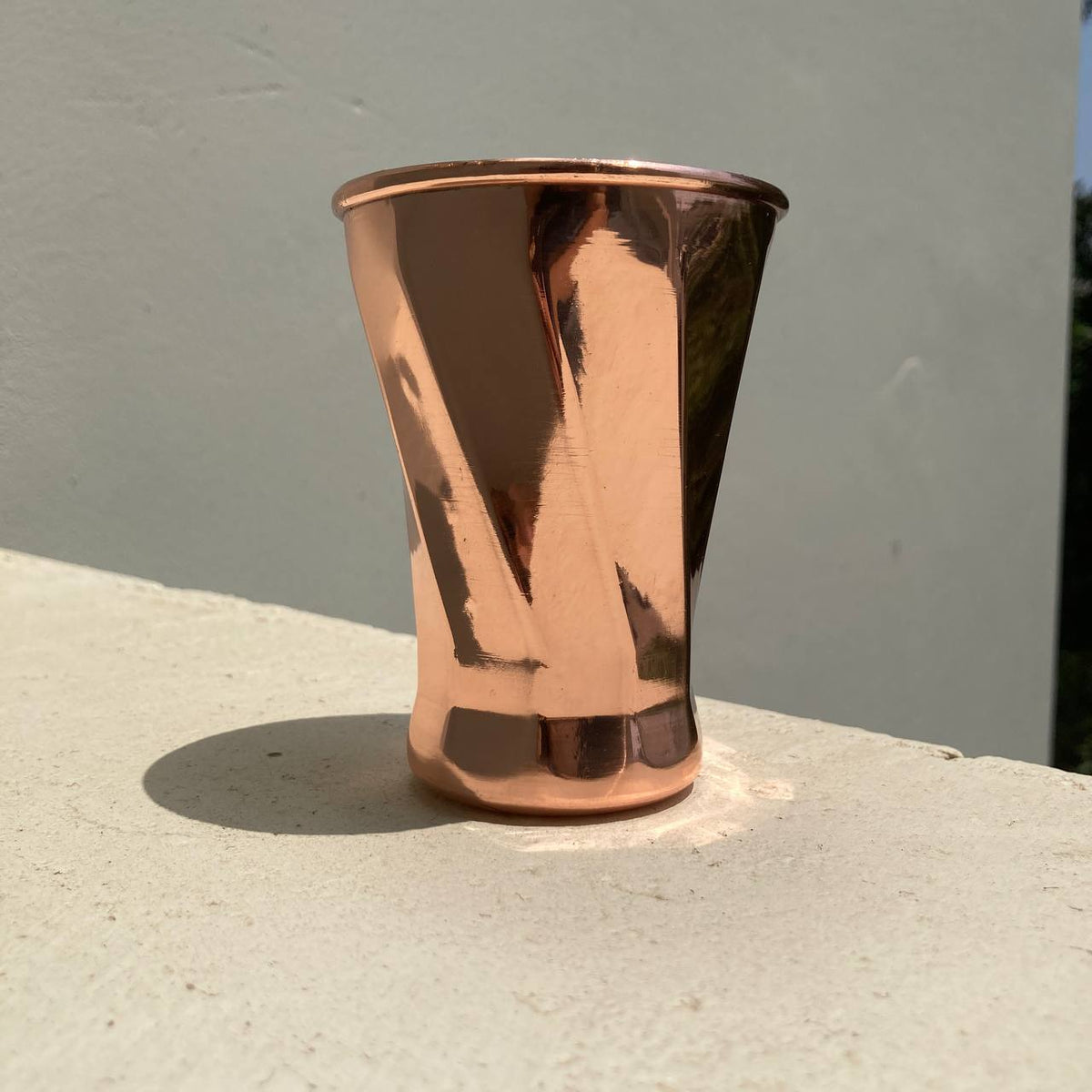 A copper-colored metal tumbler with a hammered finish, standing on a light concrete surface against a gray wall.