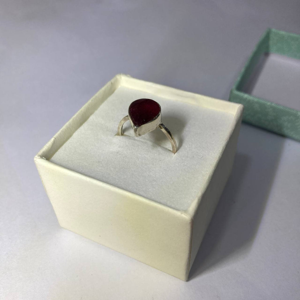 silver ring with a red ruby stone in a beige box on a light gray background