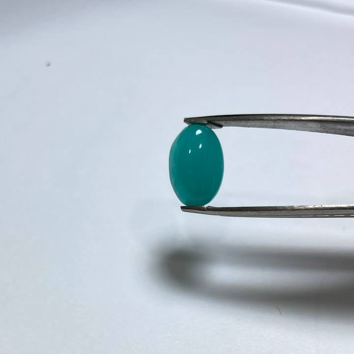 Teal gemstone held by tweezers on a white background