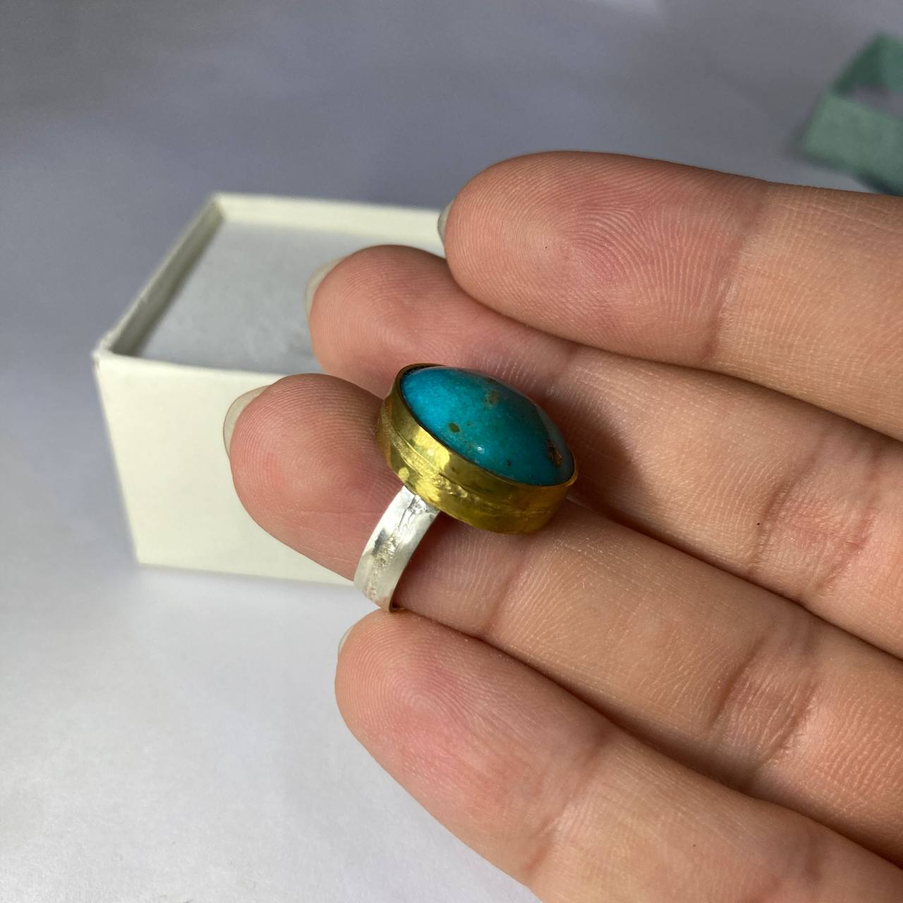silver-brass ring with a turquoise stone on a finger against a neutral background