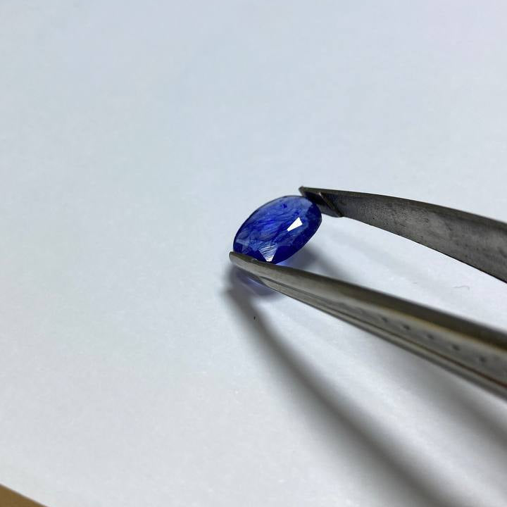 Blue gemstone held by tweezers on a white background