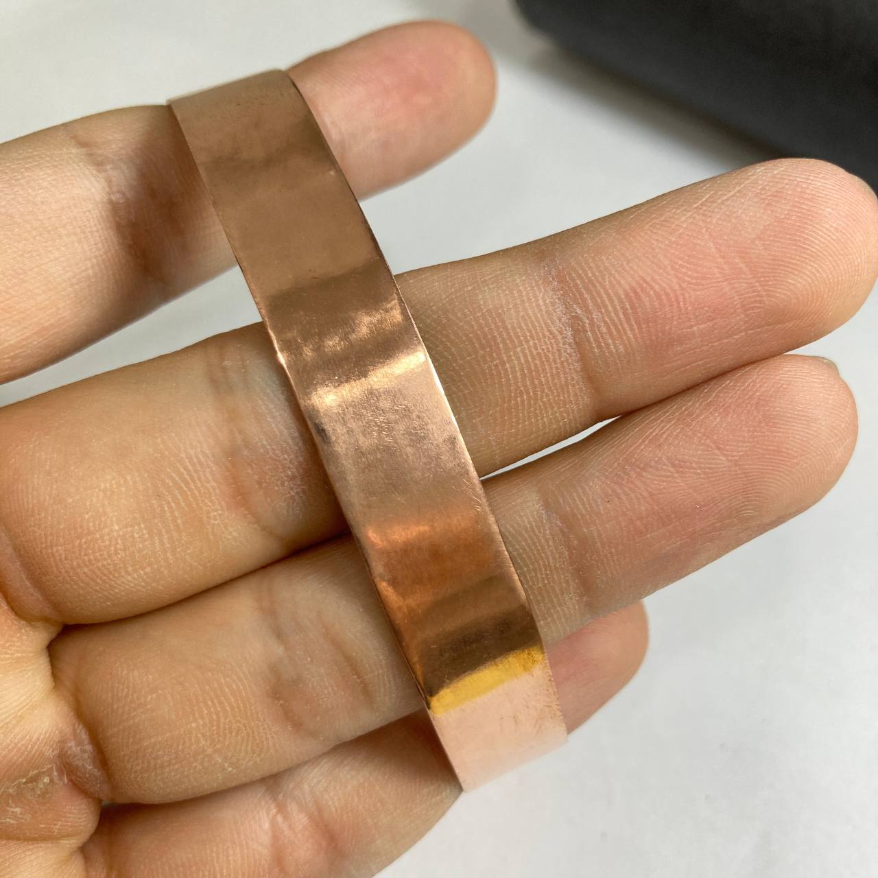 Copper strip held between fingers against a white background