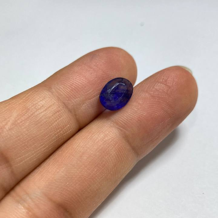 Blue gemstone held between fingers on a white background