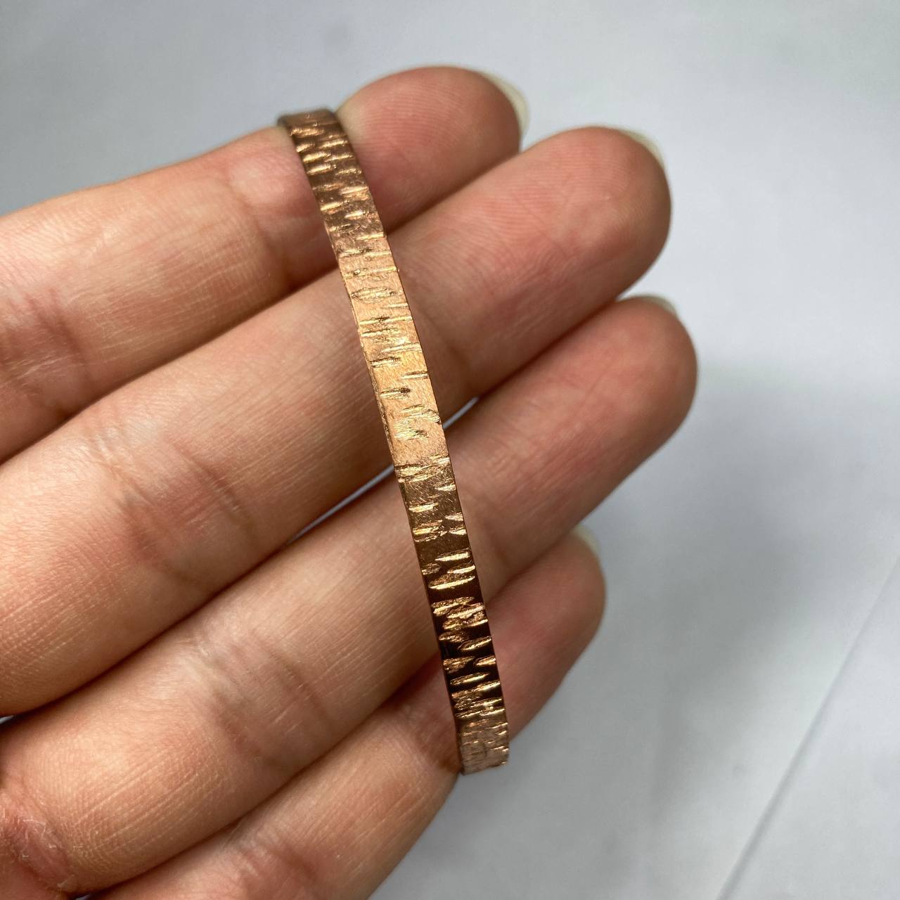 Hand holding a textured copper bracelet against a white background