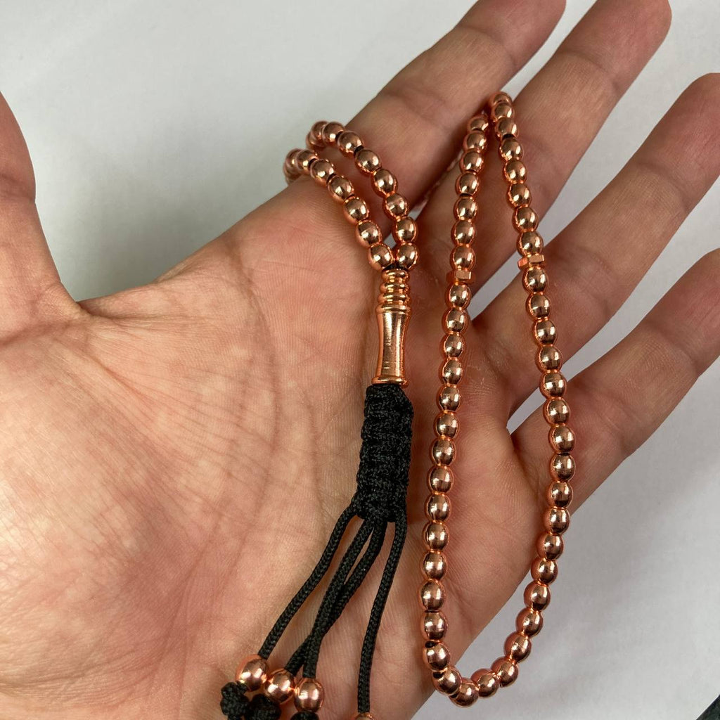 copper beaded rosary with a black braided tassel, held in a person's hand against a plain light background.