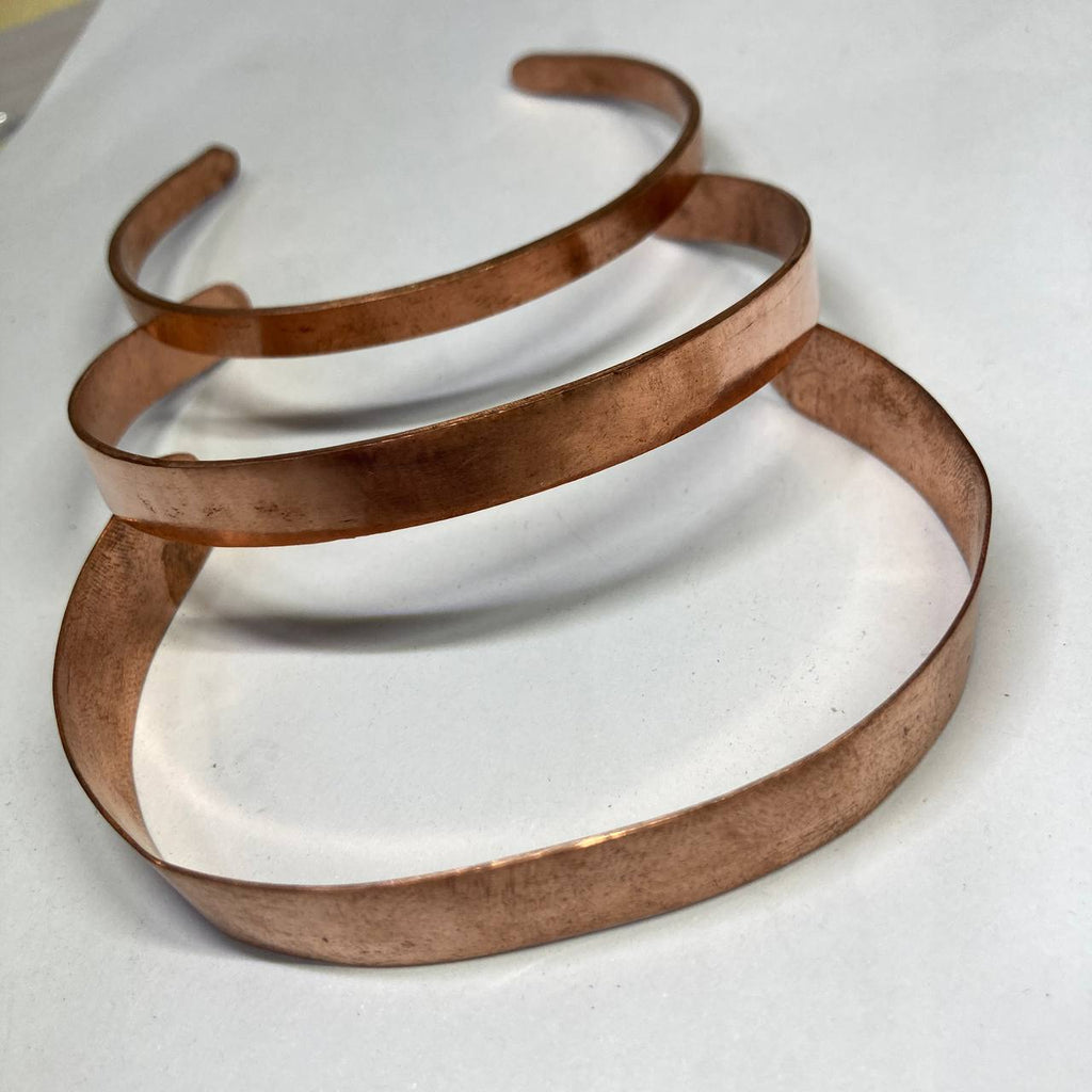 Three copper bracelets stacked on a white surface
