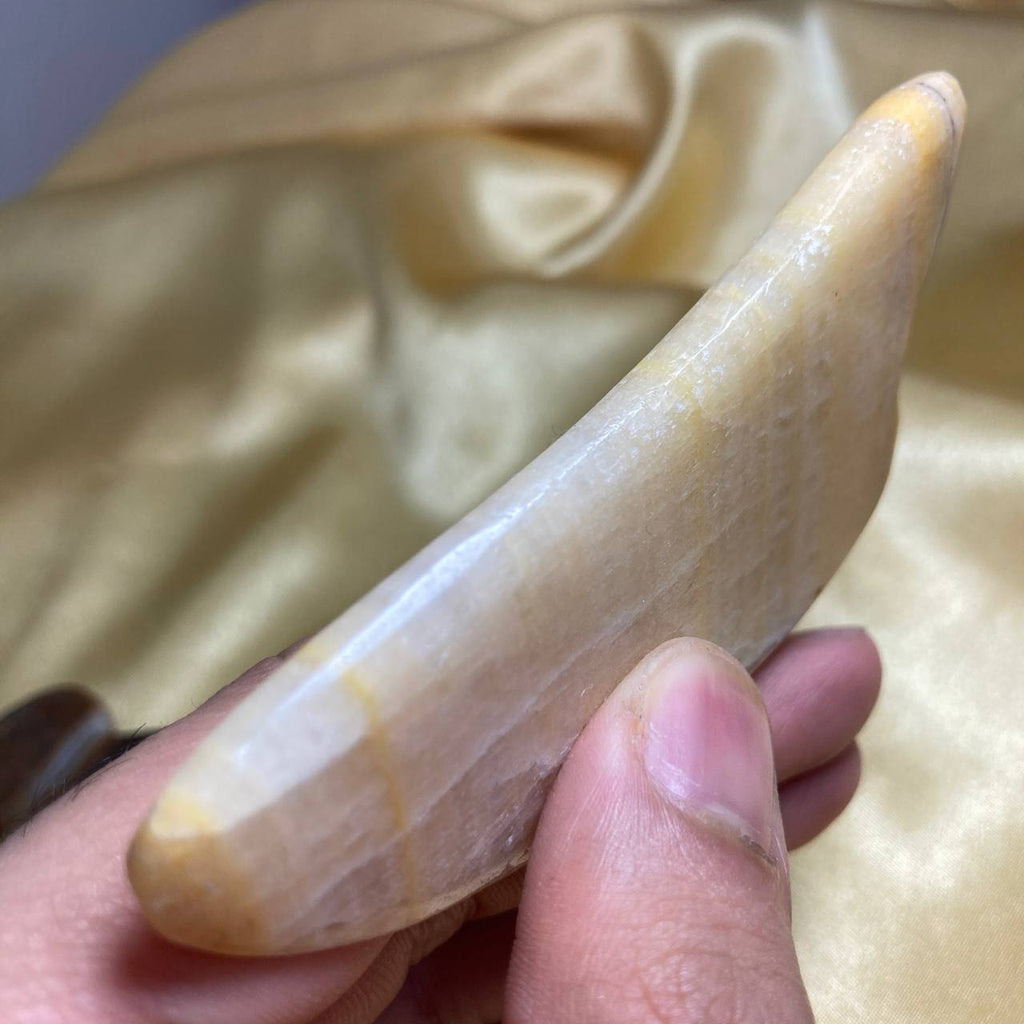 Hand holding a large, polished stone against a beige fabric background