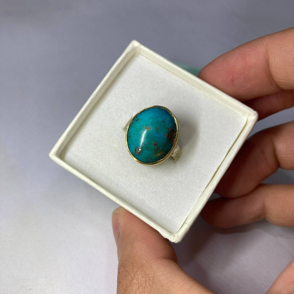 Turquoise ring in a white box held by a hand against a gray background